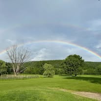 Full rainbow arching over the course with mountain backdrop