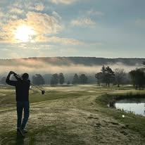 Golfer silhouette teeing off at sunrise with morning fog over the pond